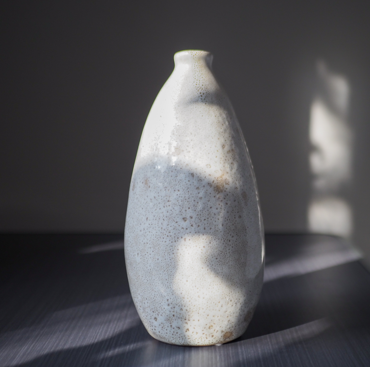 Dwa małe, ręcznie robione wazony porcelanowe w stylu japandi. Wazony mają wysokość 23 cm i pękaty kształt, dostępne w wariancie kremowym nakrapianym oraz brązowym cieniowanym. Fotografia na białym obrusie z naturalnymi dodatkami.