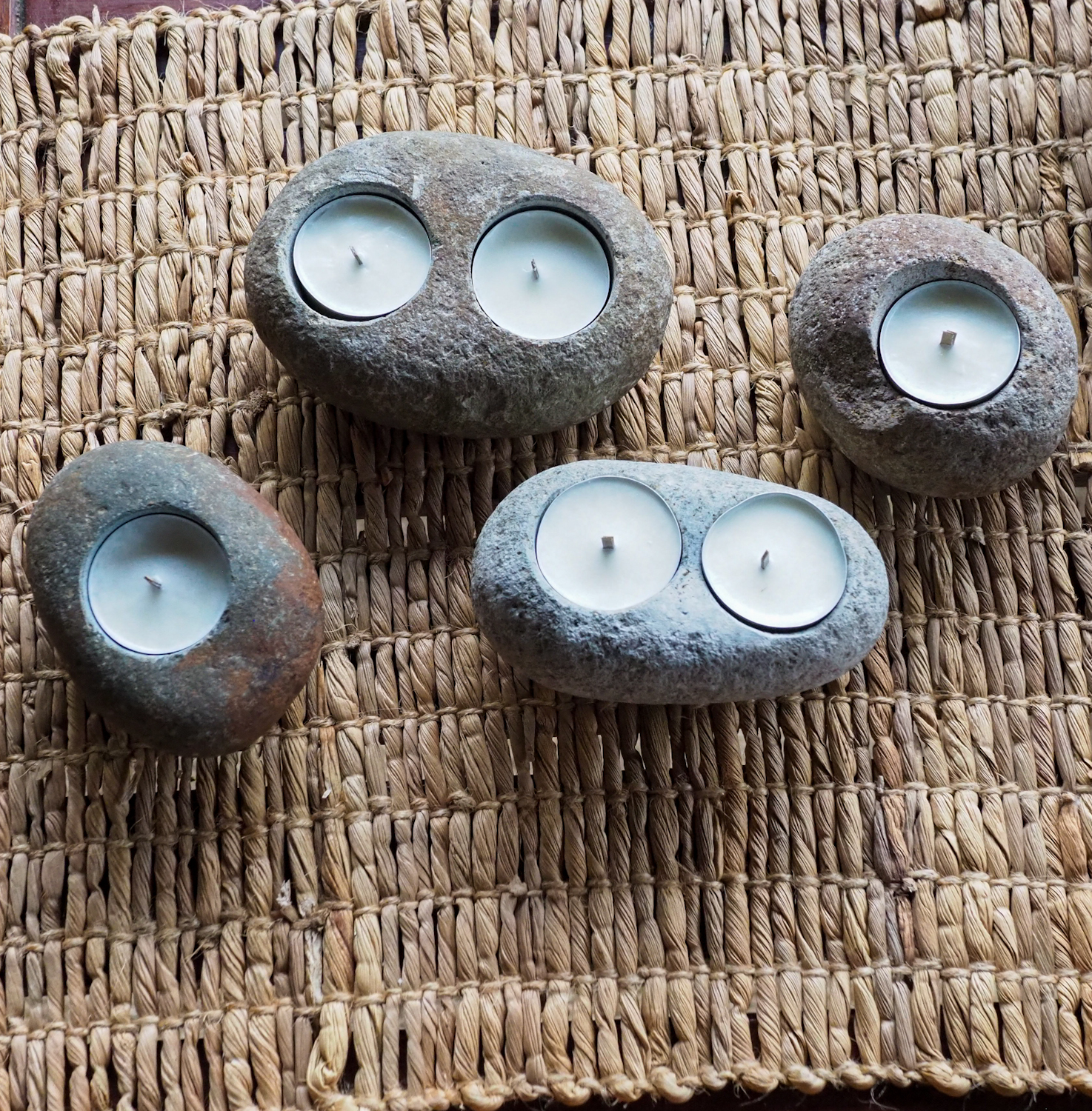 Zbliżenie na cztery unikalne świeczniki z surowych, szarych kamieni rzecznych, dwa na pojedynczy tealight, dwa na podwójny, stojące obok siebie.