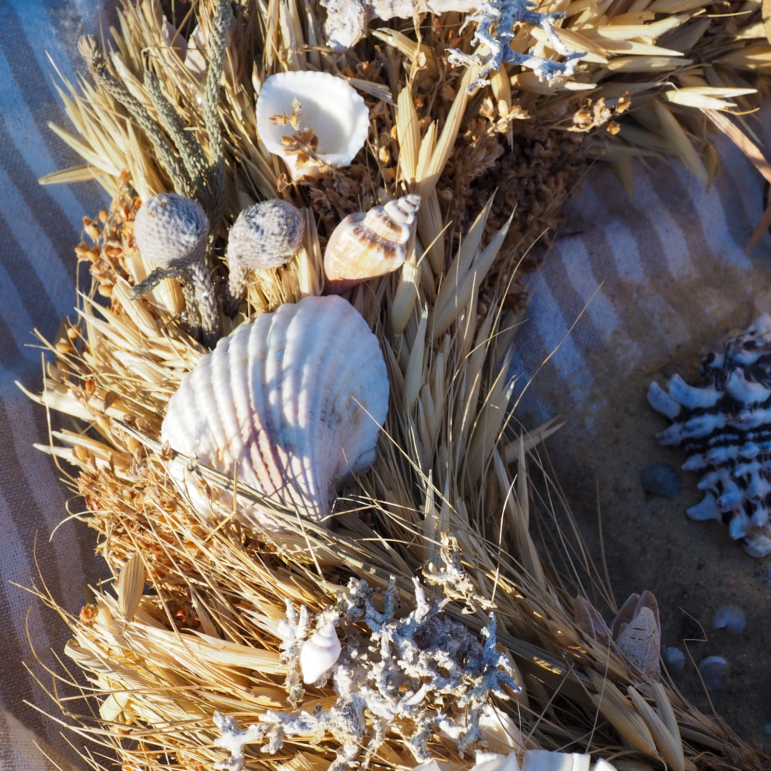 Naturalny wianek z suszonych traw i muszelek morskich THE SUMMER TIME Dream SEA leżacy na ręczniku plażowym